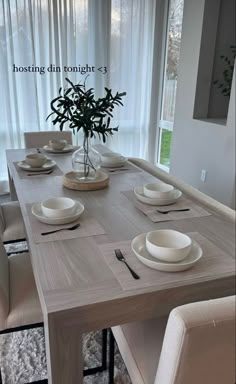 a dining room table with white plates and place settings in front of a large window