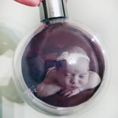 a hand holding a glass ornament with a baby in it's head