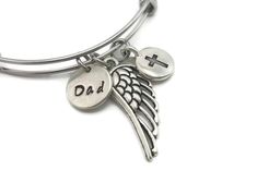 a silver bracelet with an angel wing and cross on the front, says dad in two languages