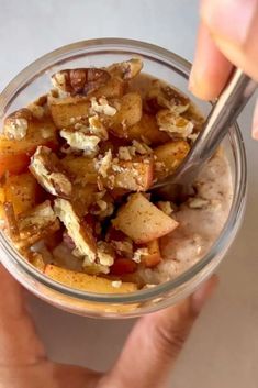 a person holding a spoon in a glass bowl filled with oatmeal and fruit