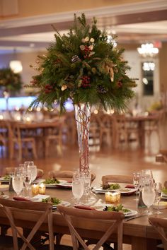 a tall vase filled with greenery sitting on top of a wooden dining room table