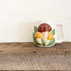 a coffee cup with mushrooms painted on it sitting on top of a wooden table next to a white wall