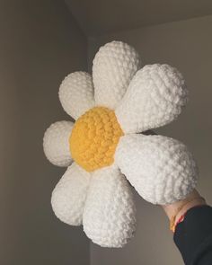 a hand holding a crocheted white and yellow flower