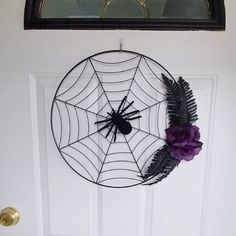 a spider web with purple flowers hanging on the front door, next to a wreath