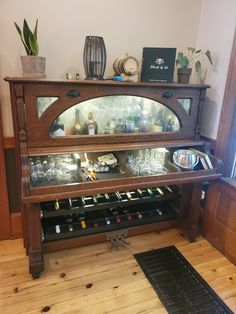 a wooden cabinet with glass shelves filled with wine bottles and other items on top of it