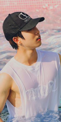 a young man sitting in the water wearing a black hat and white t - shirt