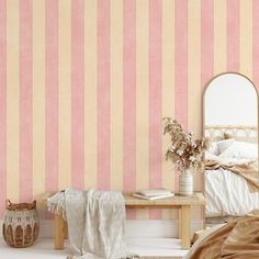 a bedroom with pink and yellow striped wallpaper next to a wooden table, mirror and wicker basket