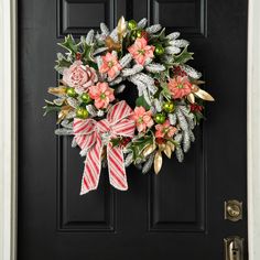 a wreath on the front door decorated with pink flowers and greenery is hanging from it's side