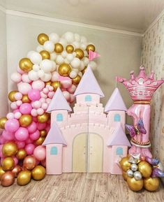 a pink princess castle with balloons in the background and a balloon wall behind it that has a crown on top