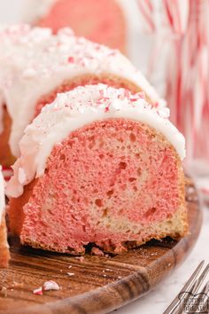 a pink cake with white frosting and sprinkles on a wooden plate