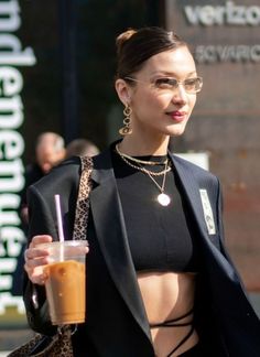 a woman wearing glasses and holding a drink in her hand while walking down the street