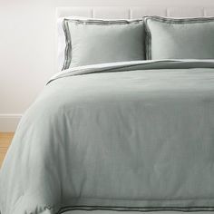 a bed with grey sheets and pillows in a room