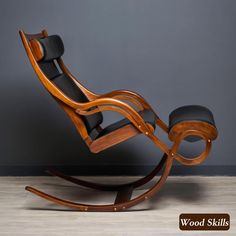 a wooden rocking chair with black leather seat and foot rest in front of a gray wall