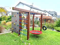 an outdoor play area with a swing set and climbing wall in the back yard, surrounded by green grass