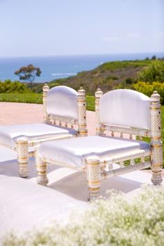 two white chairs sitting next to each other on top of a lush green field near the ocean