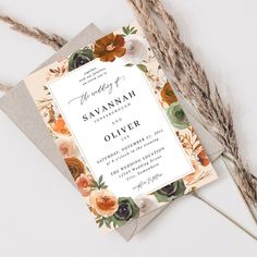 an elegant floral wedding suite is displayed on top of a card and some dried grass