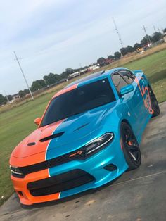 an orange and blue dodge charger parked in a parking lot next to a field