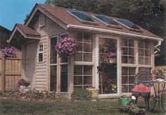 a small house with lots of windows and flowers in the front yard, next to a fence