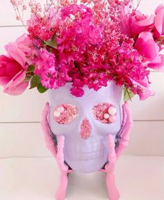 a purple skull vase with pink flowers in it