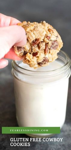 a hand holding a cookie over a jar of gluten free cowboy cookies