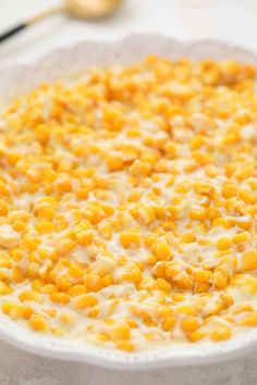 a bowl filled with corn on top of a white plate next to a gold spoon