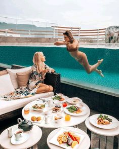 two women sitting on couches with plates of food in front of them and one woman diving into the pool