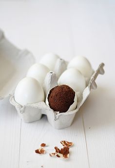 an egg is sitting in a carton next to other eggs on a white table