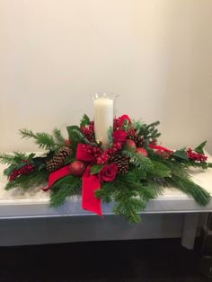 a candle sits on top of a table decorated with greenery and pine cones, red ribbon