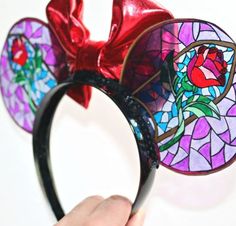 someone is holding up a stained glass mickey mouse ears headband with a red bow