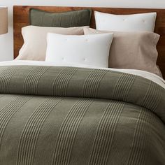 a bed with green and white comforter next to two lamps on either side of the headboard