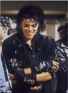 a man with black hair is smiling and holding his arms crossed while wearing leather gloves