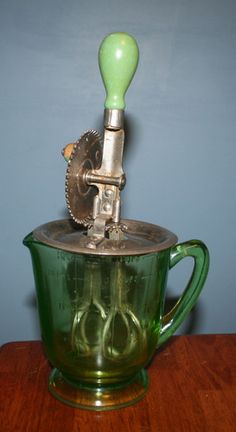 a green glass cup with an old style grinder on it's top and handle