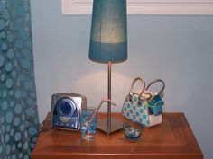 a table with a lamp and purses on it next to a blue curtained window