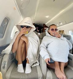 two women sitting in the back of an airplane drinking champagne and having fun with each other