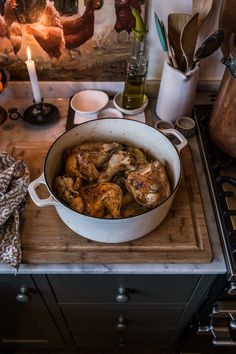 a pan filled with chicken sitting on top of a wooden cutting board next to an oven