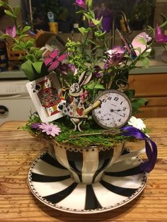 an arrangement of flowers in a teacup on top of a table with a clock