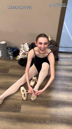 a young ballerina is sitting on the floor with her ballet shoes