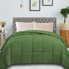 a bed with green comforter and two pictures on the wall in front of it