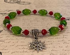 "Beautiful green glass barrel beads and vibrant red faceted glass 6mm beads are paired with a silver or gold plated snowflake charm to create an easy to wear stretch bracelet that's perfect for the holidays or anytime. The bracelet is strung on 1mm Stretch Magic cord and easily rolls over your hand to rest on the wrist. The 7.0 inch bracelet is featured in the photograph of my hand but I can custom make any size you need. Just select the size you need or convo me with your request. Please know t Christmas Bracelet Ideas, Holiday Jewelry Diy, Yule Altar, Xmas Beads, Christmas Jewelry Diy, Snowflake Bracelet, Christmas Jewellery, Christmas Tree Charm, Bead Studio