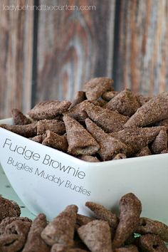 a white bowl filled with muddy brownies on top of a wooden table next to a sign that says fudge brownie blues muddy buddies