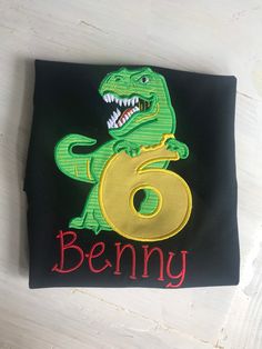 a black t - shirt with a green dinosaur on it and the number six in red