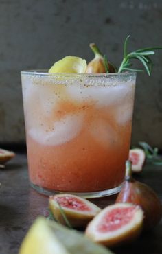 a close up of a drink on a table with figs and lemons around it