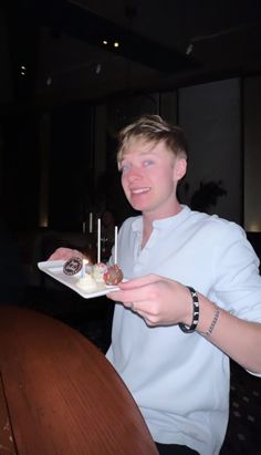 a young man is holding a plate with desserts on it and smiling at the camera