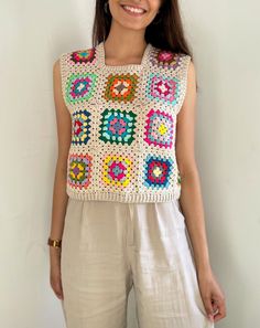 a woman standing in front of a white wall wearing a colorful crochet top