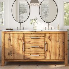 two round mirrors are above the double sink vanity in this white bathroom with wood cabinetry