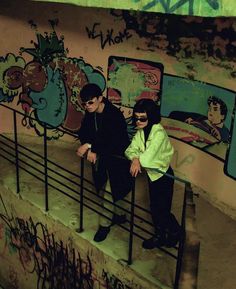 two people are sitting on some stairs in front of a wall with grafitti