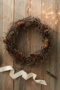 a wreath with white ribbon and pine cones on a wooden table next to some scissors