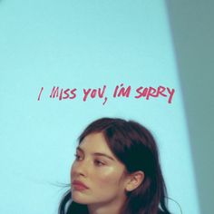 a woman with long hair standing in front of a blue wall that says miss you, i'm sorry