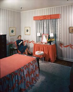 a woman sitting on a bed in a room with striped walls and red bedspread