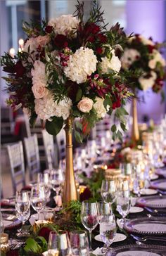 a long table is set with white and red flowers in tall gold vases on each side